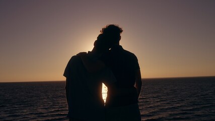 Silhouettes of gay couple enjoying romantic sunset over sea, hugging on date