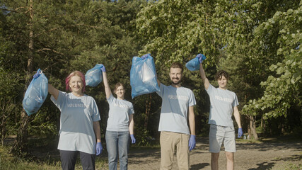Fototapeta na wymiar Happy volunteers holding bags full of trash in park, saving planet from waste