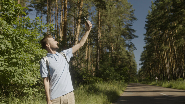 Serious man holding phone up to find mobile network in forest, tourist got lost