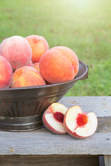 Cut peach sitting on a bench next to a colander of whole peaches outside