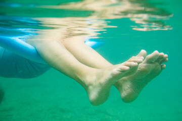 Fototapeta na wymiar close up of woman's feet underwater flowing and floating while swimming in the sea with a flotation device known as pool noodle