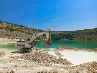 Excavator in operation on the shore of the lake, as a part of quarry rehabilitation process