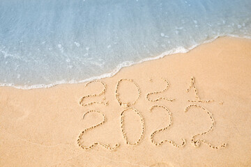 Dates written on sandy beach. 2021 washed by sea wave as New 2022 Year coming, above view