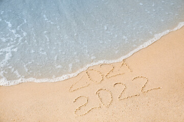 Fototapeta na wymiar Dates written on sandy beach. 2021 washed by sea wave as New 2022 Year coming