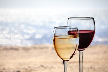 Two glasses of cold rose wine on sandy beach in sunny day,