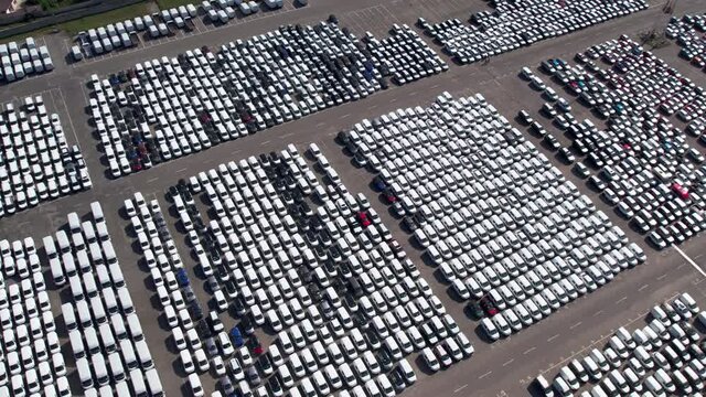 Aerial view large parking lot with new cars for sale in port of large sea city arrived by cargo ship in country drone turn automotive plant. Industrial