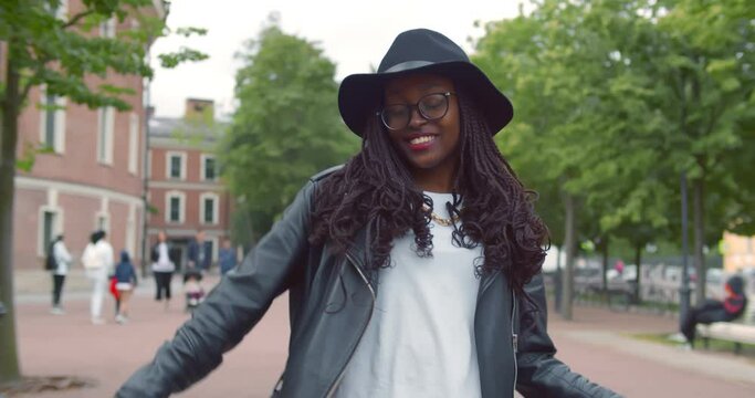 Dolly shot of pleased afro-american woman in trendy clothes dancing on street.