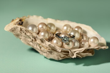 Beautiful engagement ring with gemstone and pearls in shell on mint background