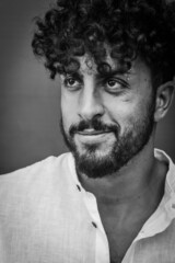 Fototapeta premium black and white portrait of a young man with beard and curly hair, who smiles slightly while looking away