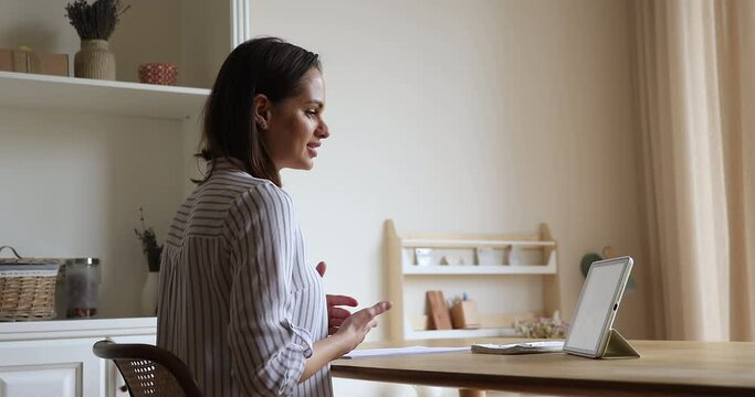 Young woman sitting in domestic kitchen using digital tablet talking by video conference application, client and counsellor lead communication remotely, working from home, video call event concept
