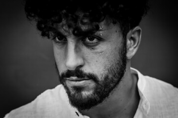 Black and white portrait of a young man with beard and curly hair who looks angry and looks...