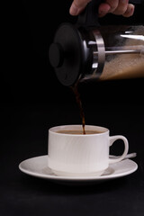 Cup of coffee and a coffee maker on black background