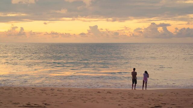 Full shot from behind of unknow couple watching sunset beach. Romantic scene man and woman stay together with carefree.