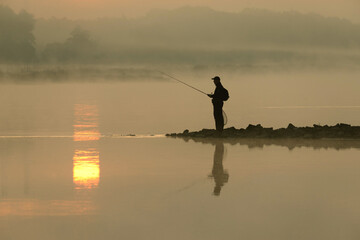 Wędkarz łowi ryby nad rzeką o wschodzie słońca latem