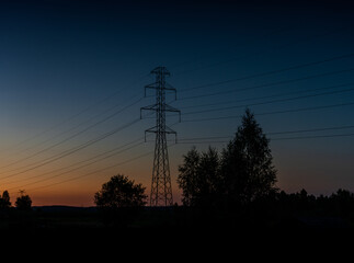 lattice cross pylon and high voltage power lines at sunset with tree silhouette in front and copy space