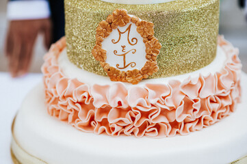 Close-up wedding cake with beautiful luxury decoration with pink frosting, golden glitters and a...