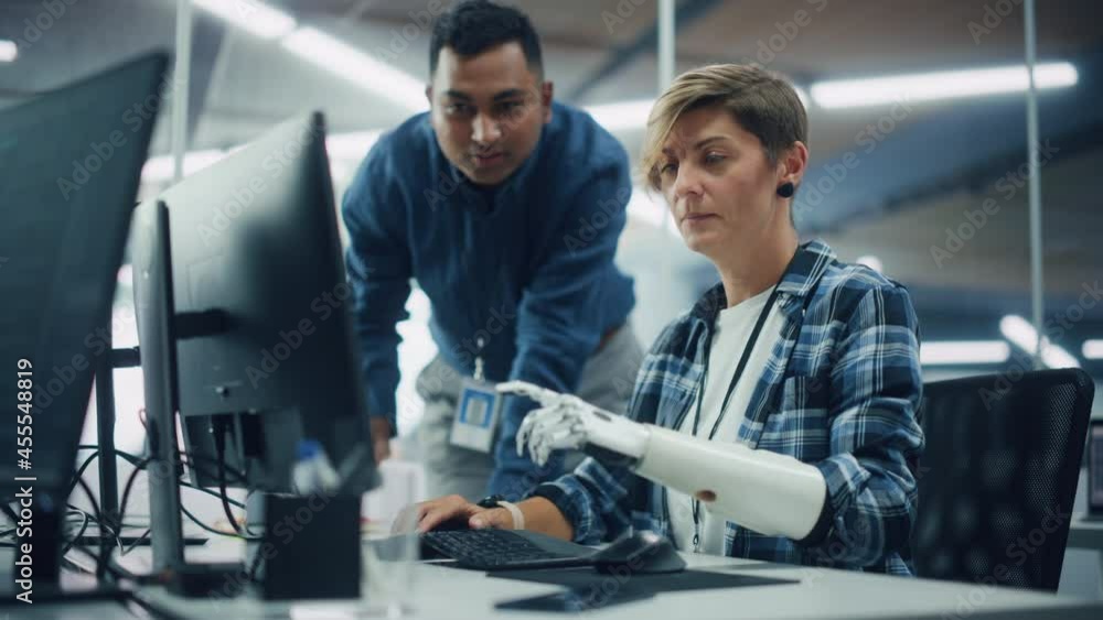 Poster Teamwork In Diverse Office: Smiling Project Manager Talks with Happy Woman with Disability with Prosthetic Arm to Work on Computer. Professionals Create e-Commerce Software App. Static Rack Focus