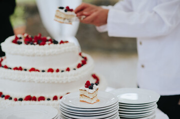 Unrecognizable waiters cutting wedding cake to serve guests during banquet in a restaurant. Three layers cake.
