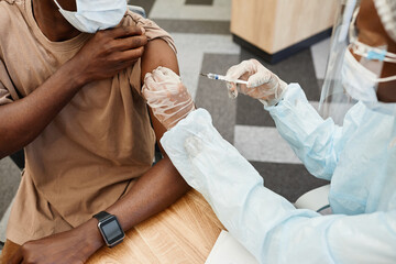 Doctor in PPE suit giving second shot of vaccine against coronavirus to male patient in clinic © Seventyfour