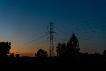 lattice cross pylon and high voltage power lines at sunset with tree silhouette in front and copy space