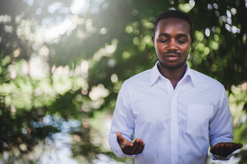 African man praying for thank god with light flare and beautiful bokeh in green nature background