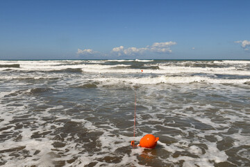 Seascape with orange buoys on big waves and clear blue sky, Tuscany, Italy