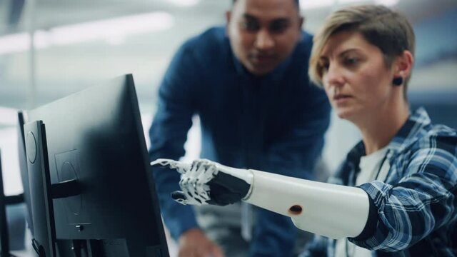 Teamwork In Diverse Office: Smiling Project Manager Talks with Happy Woman with Disability with Prosthetic Arm to Work on Computer. Professionals Create e-Commerce Software App. Rack Focus on Hand