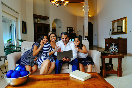 Happy family waving while attending online prayer video call through laptop sitting on sofa in living room at home