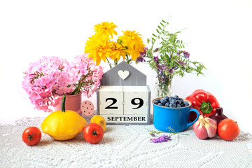 Calendar for September 29 : the name of the month in English, cubes with the number 29, ripe vegetables, bouquets of various flowers, blueberries in a blue cup on a gray napkin, white background