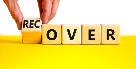 Time to recover symbol. Businessman turns a wooden cube and changes the word 'over' to 'recover'....