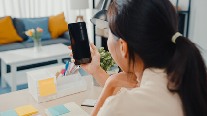 Young Asia lady use smart phone with blank black screen mock up display for advertising text while smart working from home at living room. Chroma key technology, Marketing design concept.