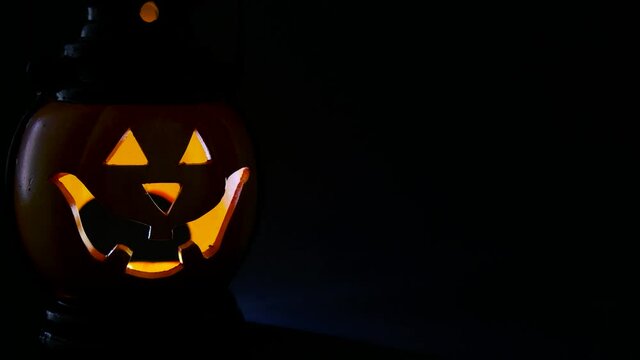 Halloween, horror and mysticism concept. Flickering glowing orange pumpkin with carved face in the dark, alloween background, place for text, copy space