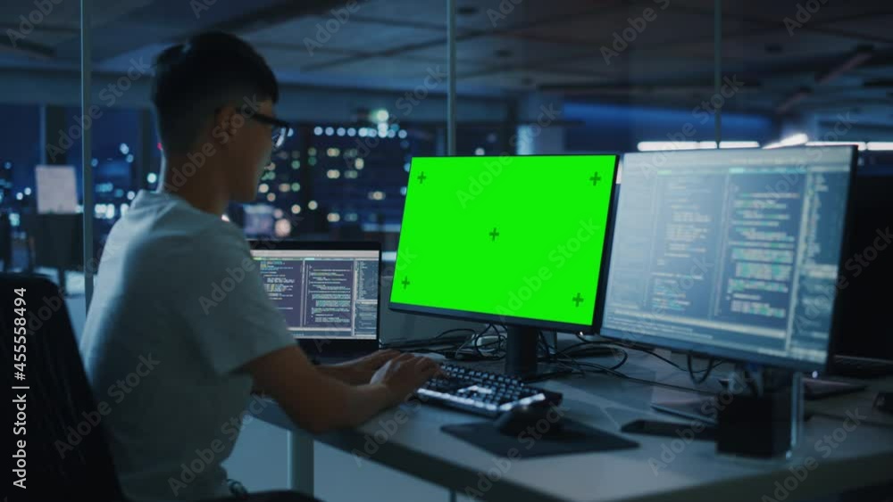 Poster Night Office: Young Japanese Man in Working on Green Screen Chroma Key Desktop Computer. Programmer Typing Code, Creating Modern Software, e-Commerce App Design. Over Shoulder