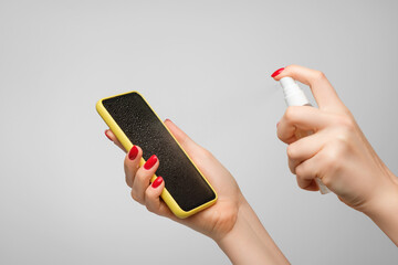 Woman's hands spray disinfectant on mobile phone to clean and protect against viruses. Cleaning...