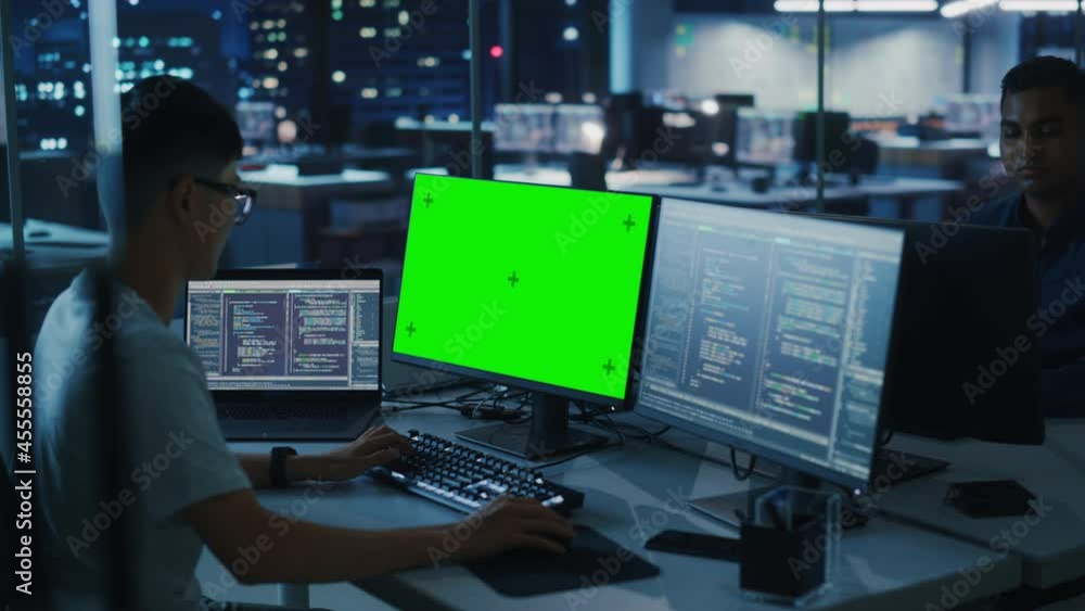 Aufkleber Night Office: Young Japanese Man in Working on Green Screen Chroma Key Desktop Computer. Team of Programmers Typing Code, Creating Modern Software, e-Commerce App Design, e-Business Programming