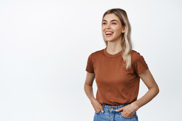 Obraz premium Young happy woman with blond hair, looking aside with friendly smile, talking to someone and laughing, standing against white background