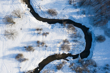 Drone shot flying on forest and river in winter, aerial top-down view.