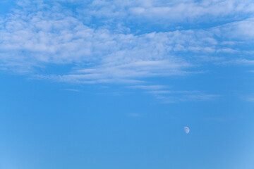 Blue sky background with white clouds and the moon