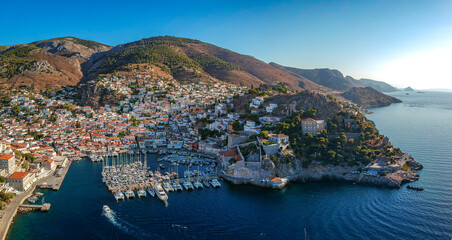 Naklejka premium Aerial drone panoramic photo of the picturesque port and main village of Hydra (or Ydra) island at sunset. Hydra is a top tourist destination with neoclassic houses located in Saronic gulf, Greece.