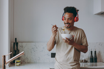Young african american man in casual clothes headphones listen music eat breakfast muesli cereals...