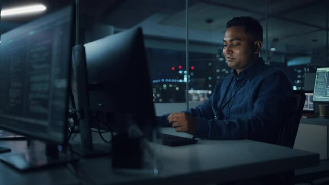 Night Office: Portrait of Handsome Indian Man in Working on Desktop Computer. Digital Entrepreneur Typing, Creating Software, e-Commerce App Design, Programming. Thoughtful Happy Man Finding Solution