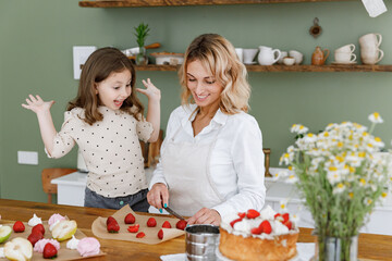 Happy chef cook baker mom woman in white shirt work with fun baby girl helper teach baking spread...