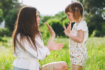 Obraz premium Happy smiling young woman in white clothes have fun with cute child baby girl 5-6 years old Mommy play clap your hands rest with little kid daughter outdoor together. Mother's Day love family concept