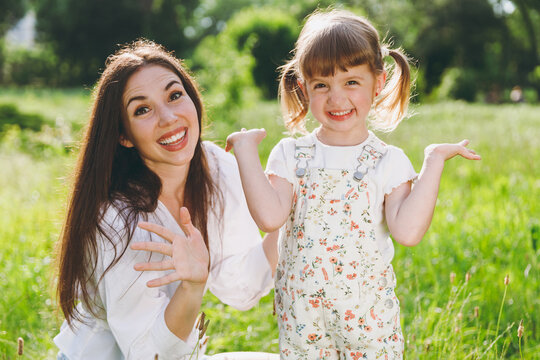 Happy smiling young woman in white clothes have fun child baby girl 5-6 years old, spread hands. Mommy play rest with little kid daughter spend time outdoor together. Mother's Day love family concept