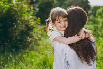Lovely cute young woman wearing white clothes have fun hugging child baby girl 5-6 years old. Mommy rest with little kid embrace daughter spend time outdoor together. Mother's Day love family concept