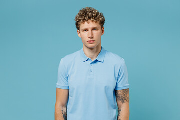 Young beautiful businesslike calm curly man 20s years old wears azure t-shirt posing looking camera isolated on plain pastel light blue background studio portrait. People emotions lifestyle concept.