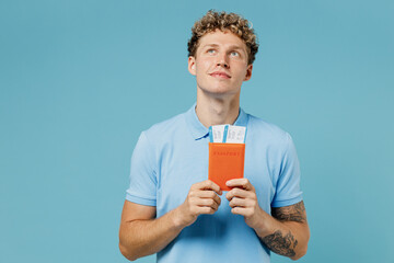Traveler tourist puzzled young curly man 20s wears azure t-shirt hold passport boarding pass ticket look up isolated on plain pastel light blue background studio portrait.Air flight journey concept. - obrazy, fototapety, plakaty