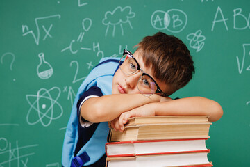 Young sad tired male kid school boy 5-6 years old in t-shirt backpack glasses lying on books...