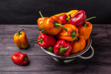 Colorful sweet peppers in a colander on a wooden table