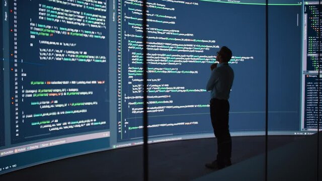 High-Tech Startup Concept: Innovative Male Software Engineer Standing, Doing Big Data Analysis on Wall Screen Showing Porgramming Code. Developing Futuristic e-Commerce App with Machine Learning. Full